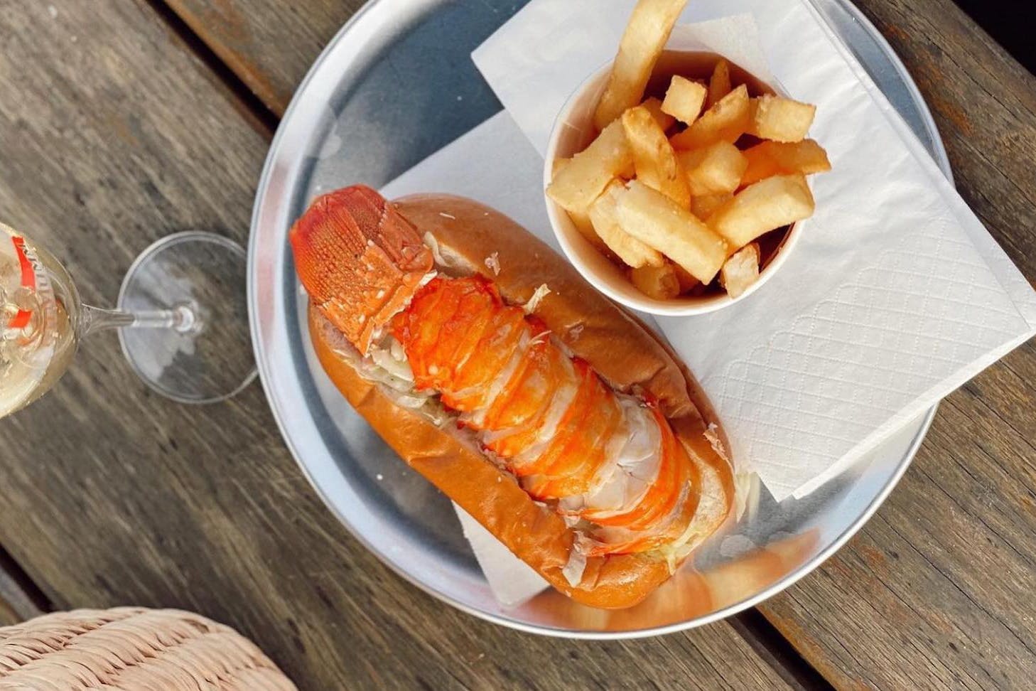 A lobster tail on a roll with chips and a glass of champagne.